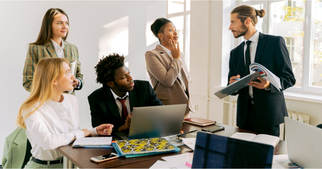 Business professional in a navy suit, presenting documents to a team of four