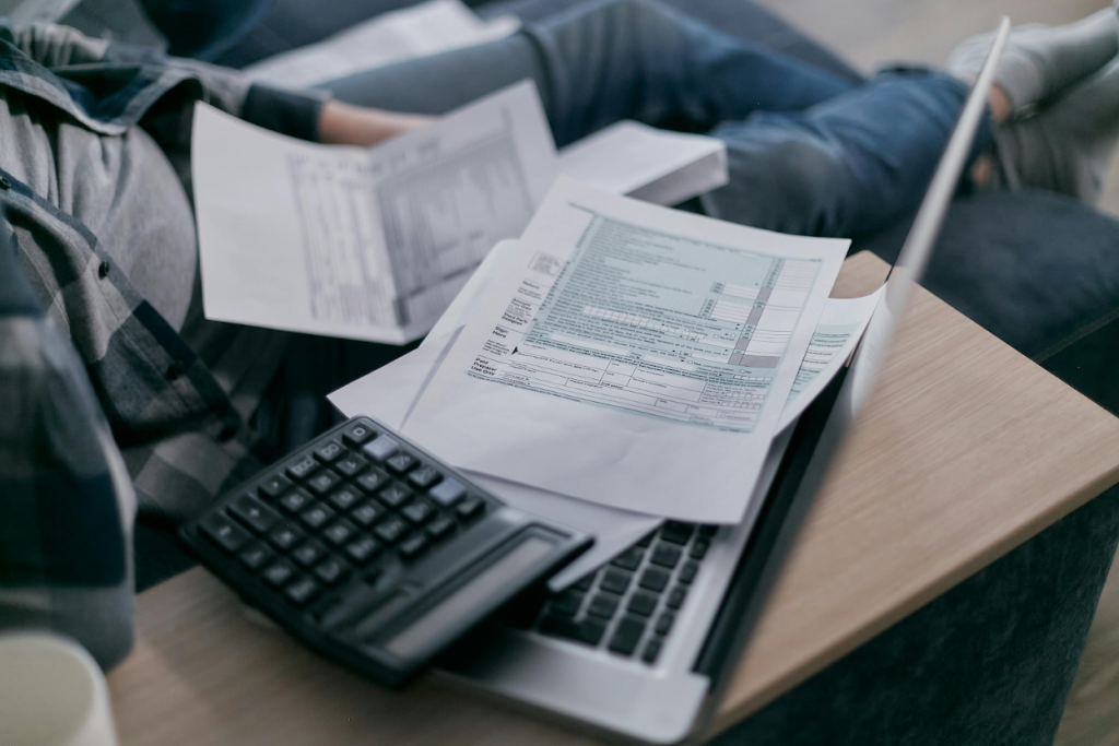 Person reviewing financial documents and bills on a laptop with a calculator nearby.