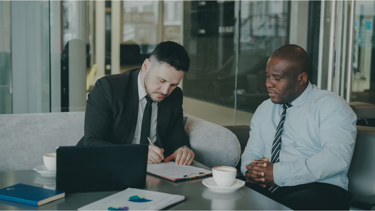 Two businessmen signing a document on a table