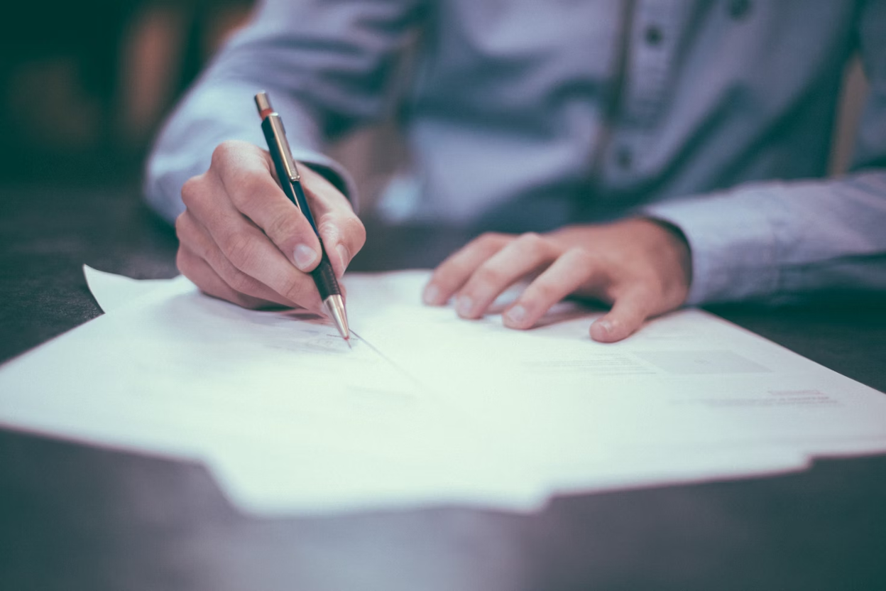 A businessman in a suit sits at his desk signing some documents.