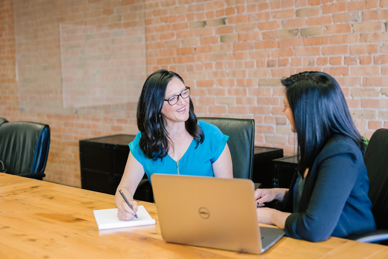 A woman in a teal blouse sitting and talking to a woman in a suit jacket