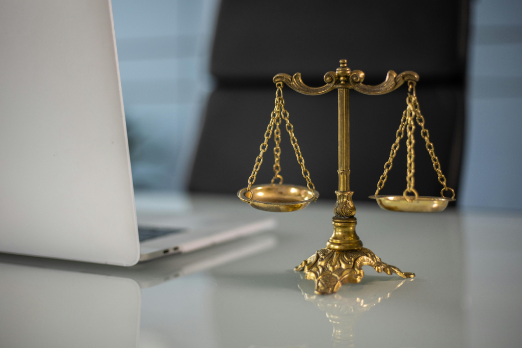 Golden scales of justice on a desk with a laptop in the background