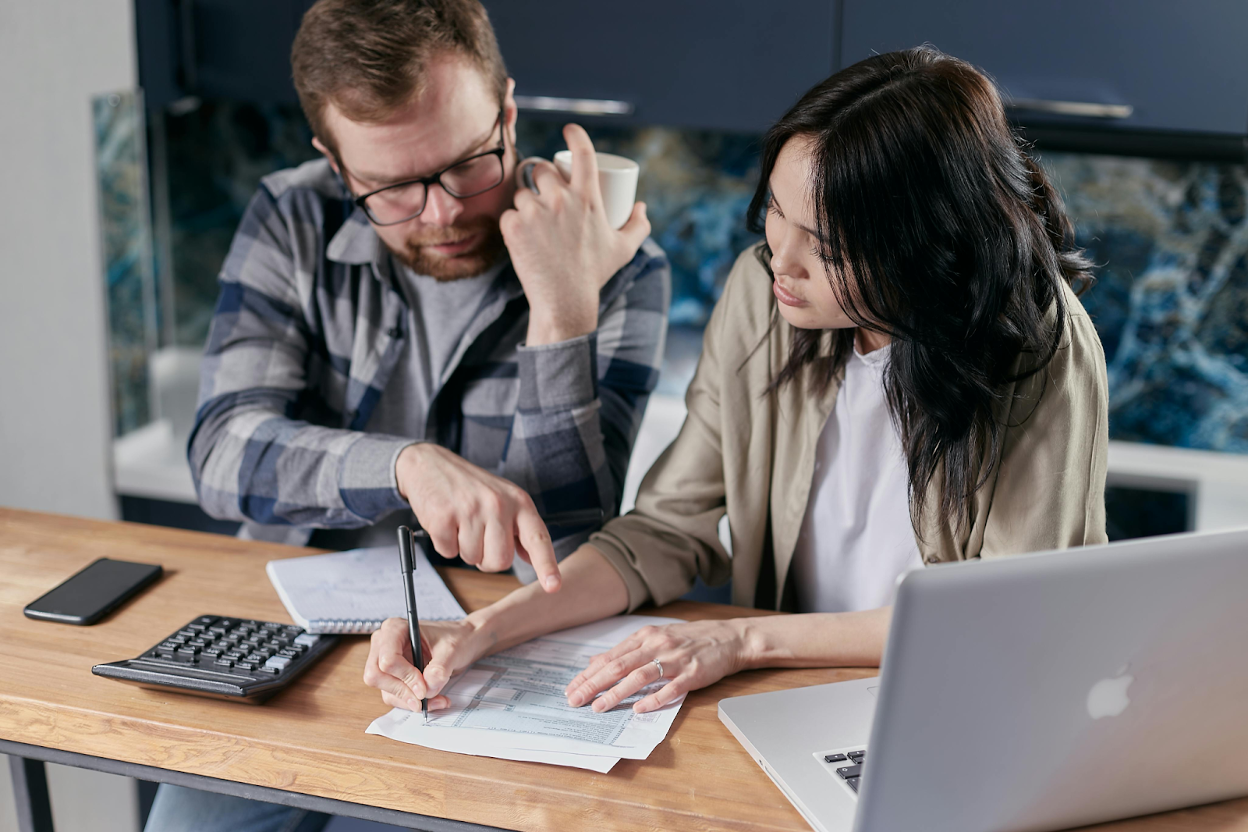 Two people reviewing financial documents with a laptop and calculator