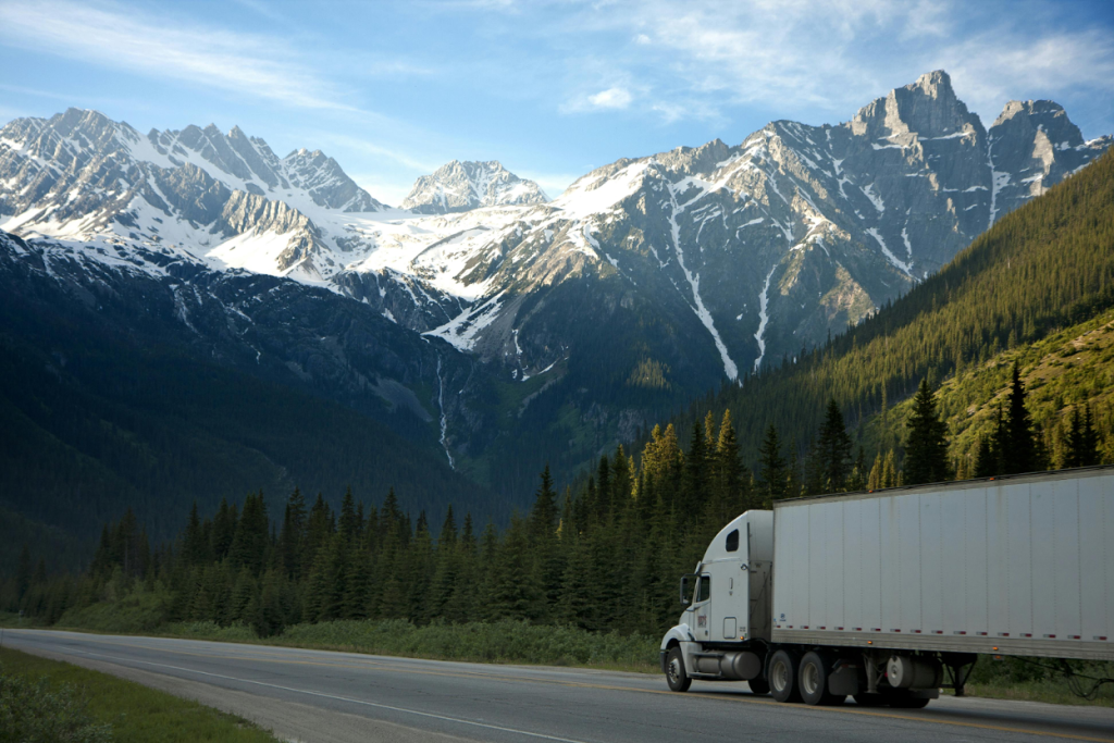 White semi-truck with trailer driving on a highway through mountainous terrain
