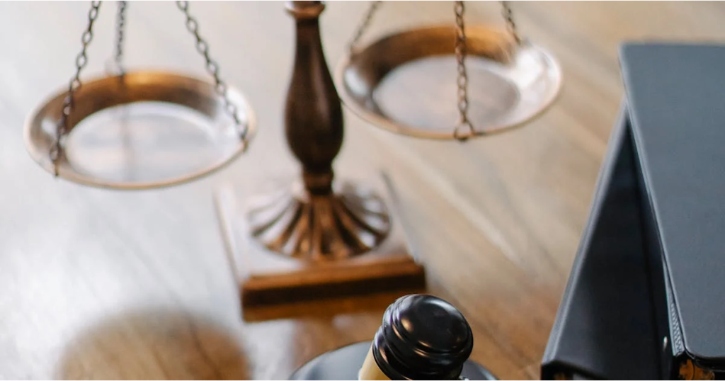 A close-up of a judge's gavel resting on a wooden surface beside legal books, with scales of justice blurred in the background