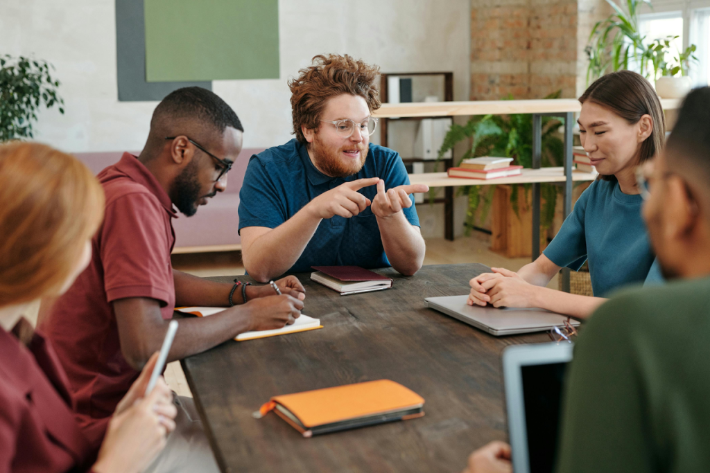 A team having a meeting around a wooden table in a modern office with plants, notebooks, and natural lighting