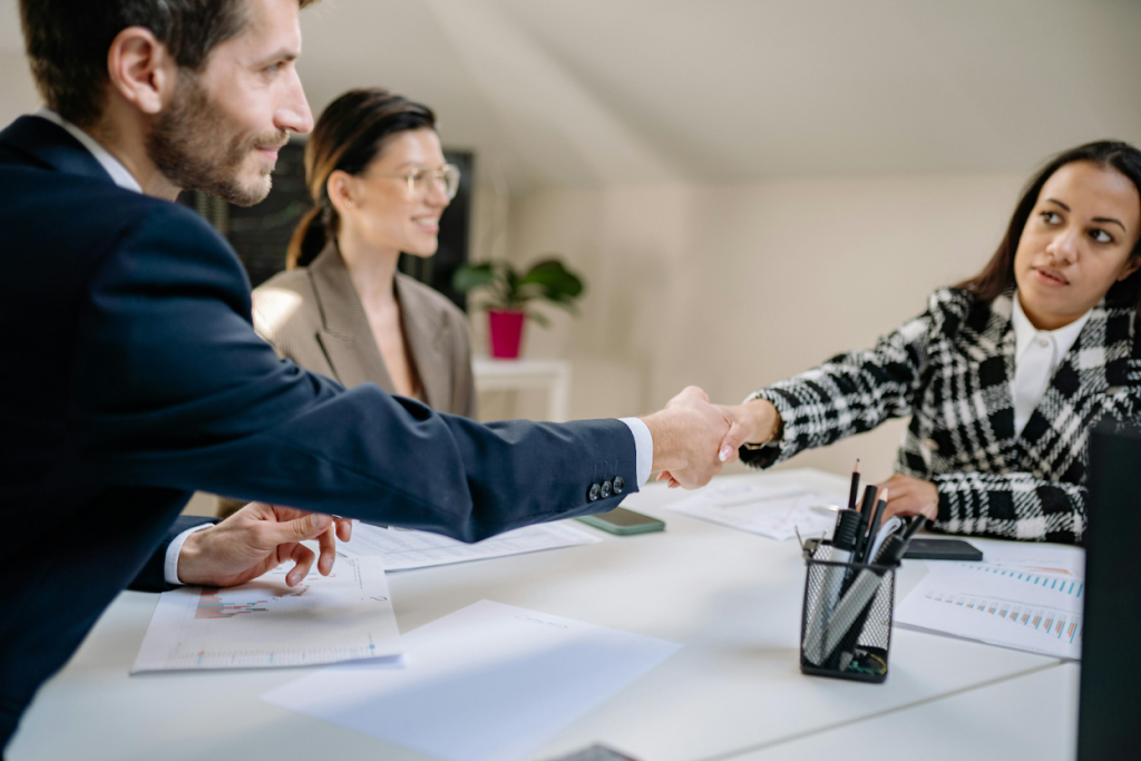 Business professionals shaking hands across a conference table during a meeting.