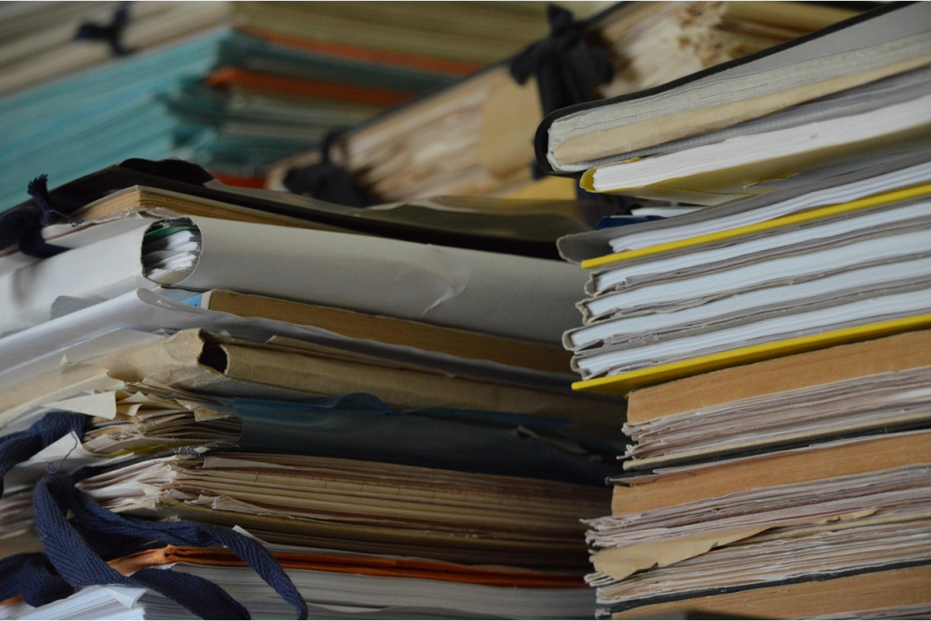 Close-up photograph of stacks of worn books, folders, and bound documents