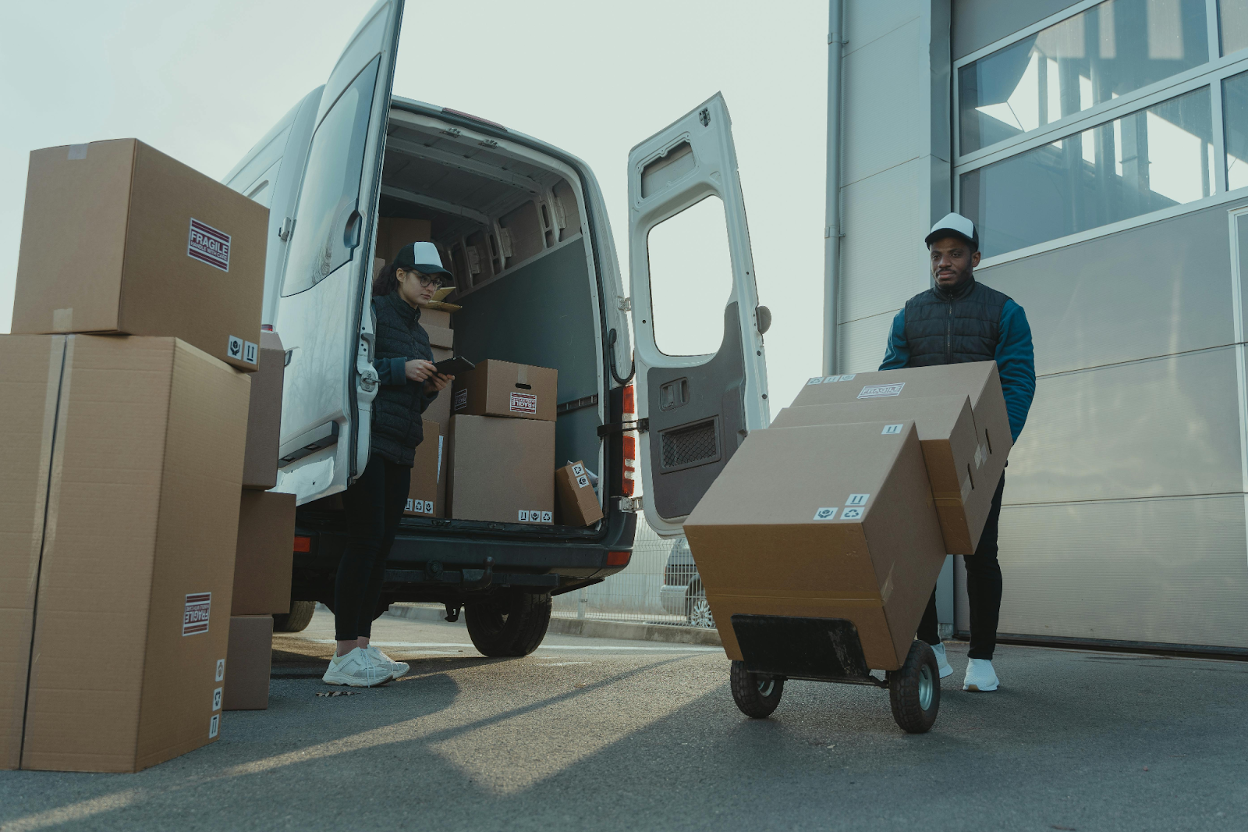 Delivery workers unloading cardboard boxes from a white delivery van