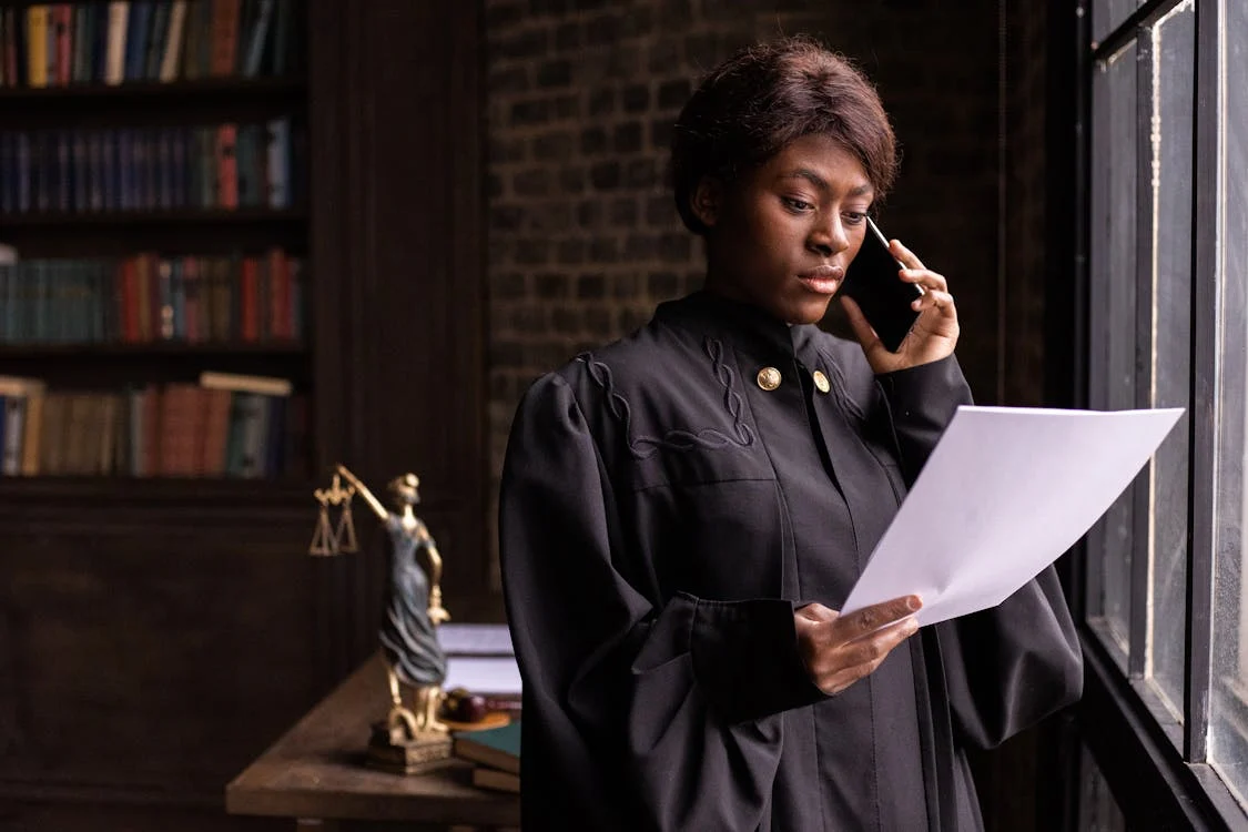 Female judge in black judicial robes standing in a law office, holding a phone to her ear