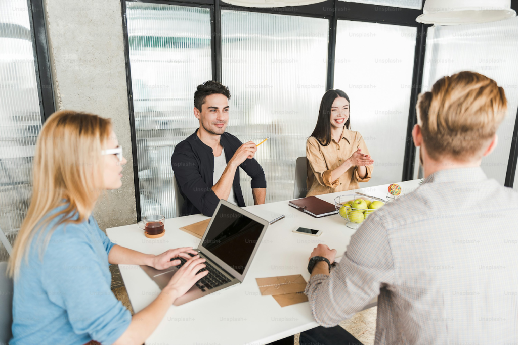 Four business professionals are having a collaborative meeting around a white table in an office