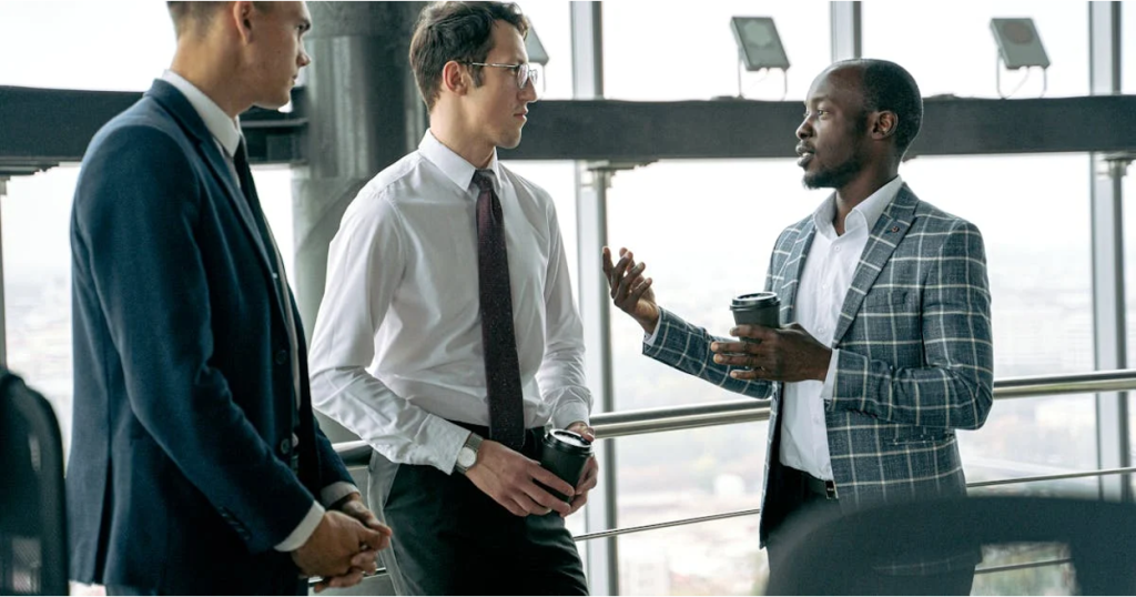 Three business professionals in suits discussing in a modern office.