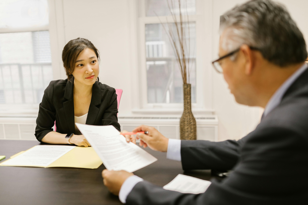 Two business professionals in suits reviewing documents across a desk in an office setting