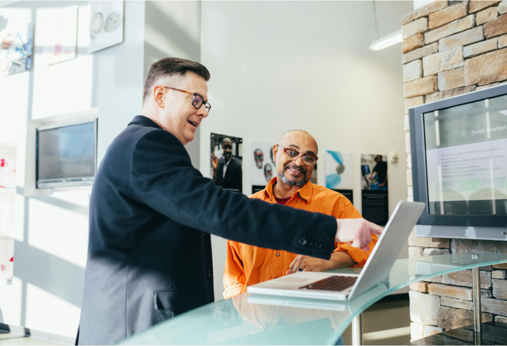 Two businessmen in a modern office collaborating at a laptop on a glass desk