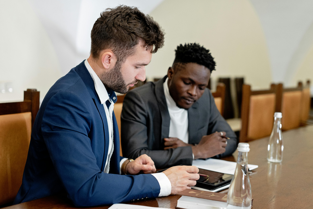 Two businessmen in suits sitting at a conference table reviewing documents.