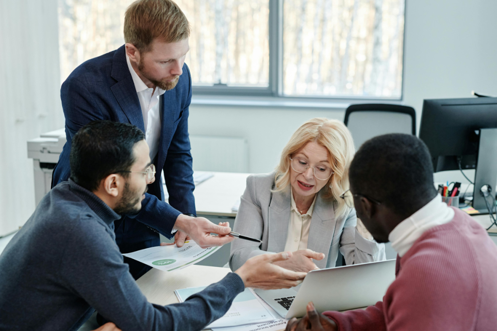 Four business professionals collaborating around a laptop and documents at an office desk