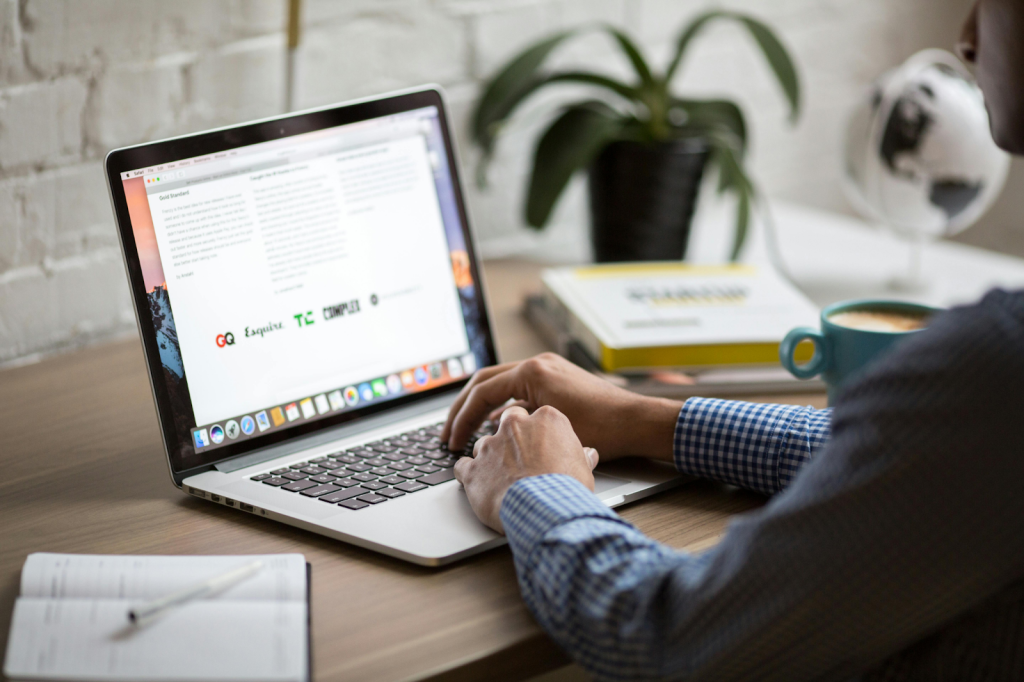 Person in a blue checkered shirt typing on a MacBook.