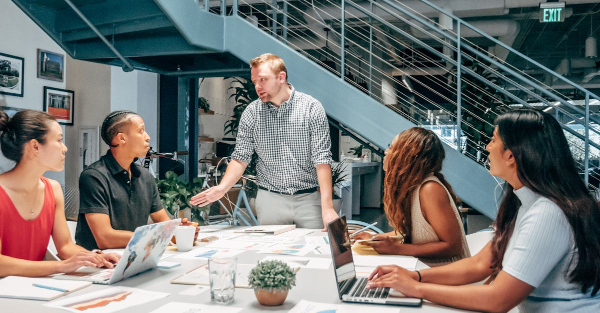 Team member presenting to colleagues during a meeting in a modern open-plan office with laptops and charts.