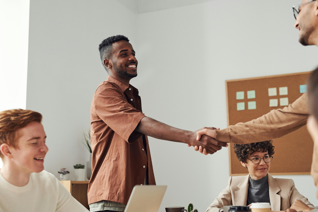 Team members greet with a handshake in a casual office meeting.