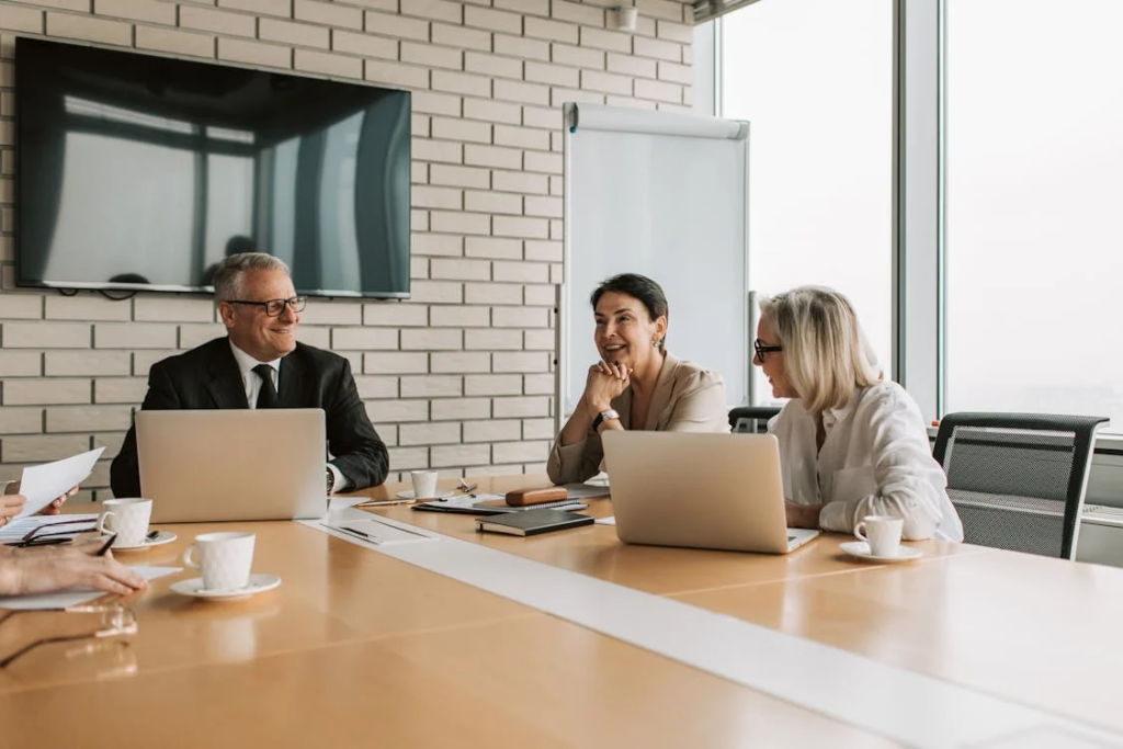 Three business professionals having a meeting at a conference table with laptops.