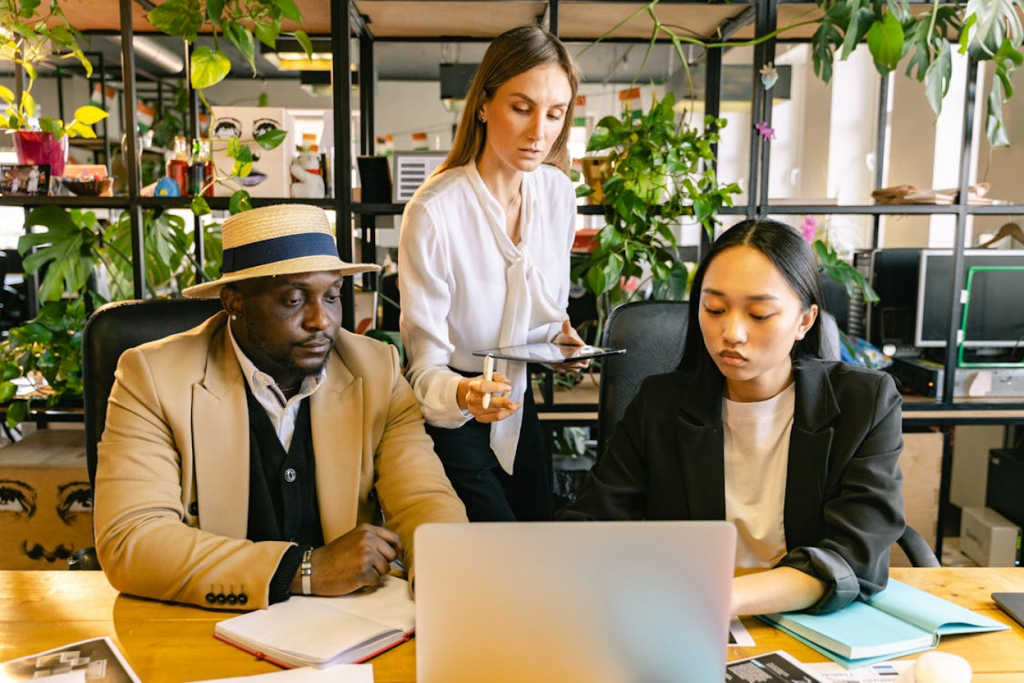 Three professionals collaborating around a laptop in a modern office with plants