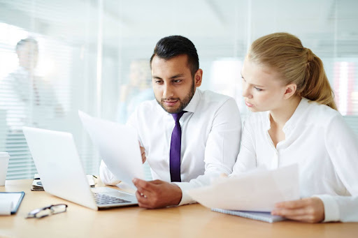 Two business professionals reviewing financial documents and contracts at a conference table.