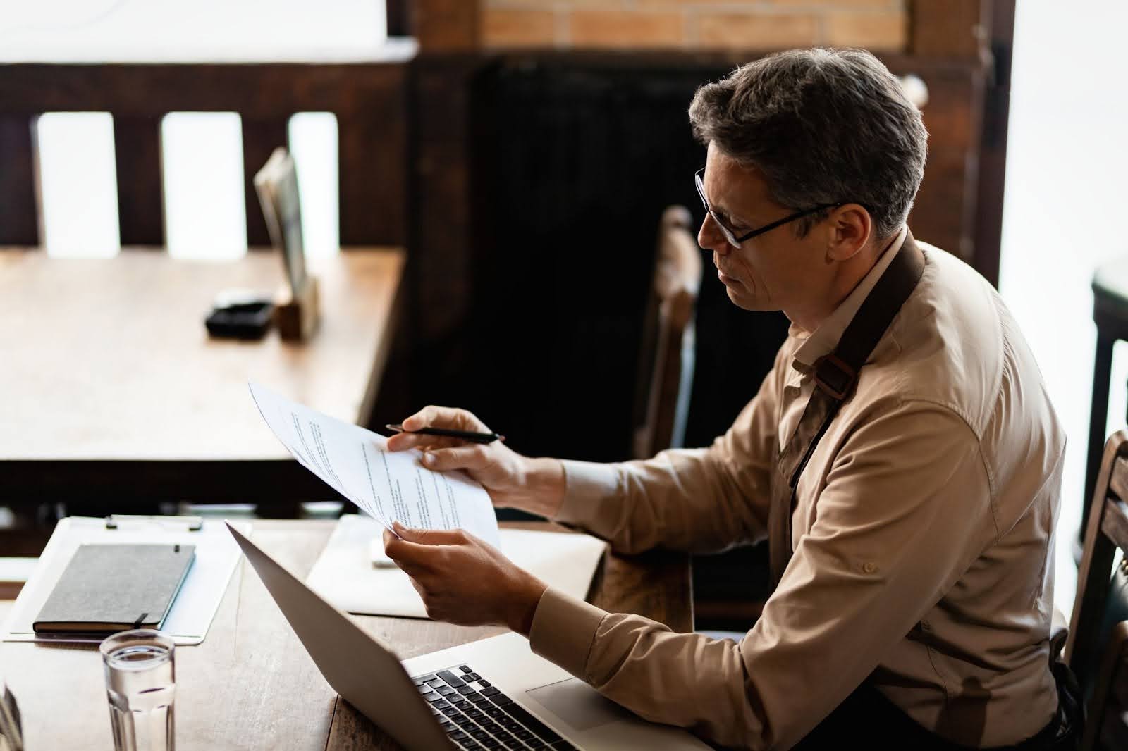 Business owner analyzing financial documents and invoices at a desk with a laptop.