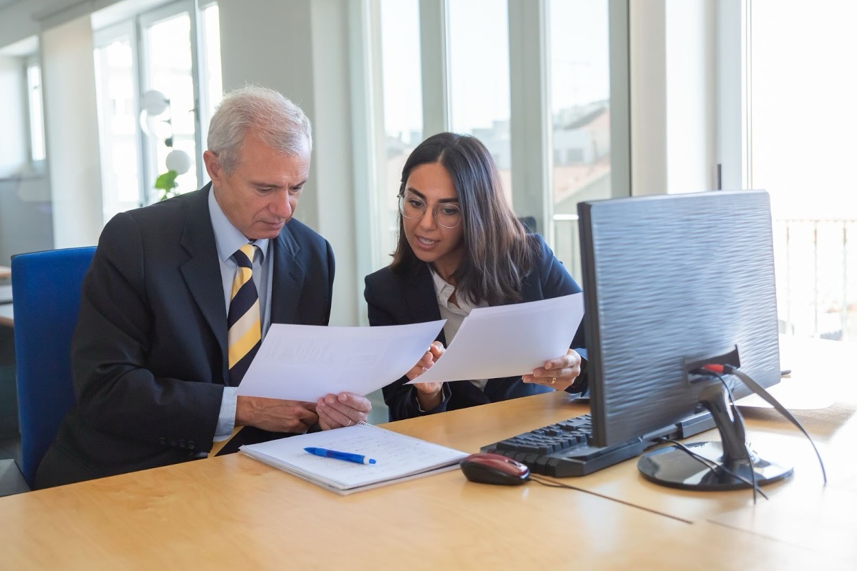 Business professionals reviewing financial documents and invoices in a modern office conference room setting.