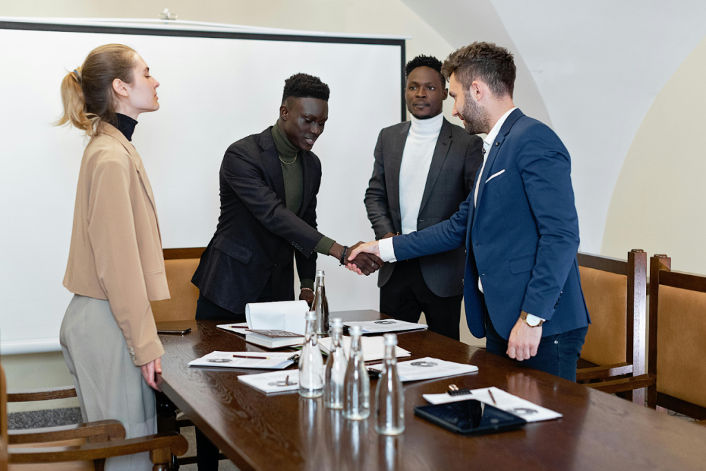 Business professionals shaking hands across a conference table while colleagues observe during a meeting