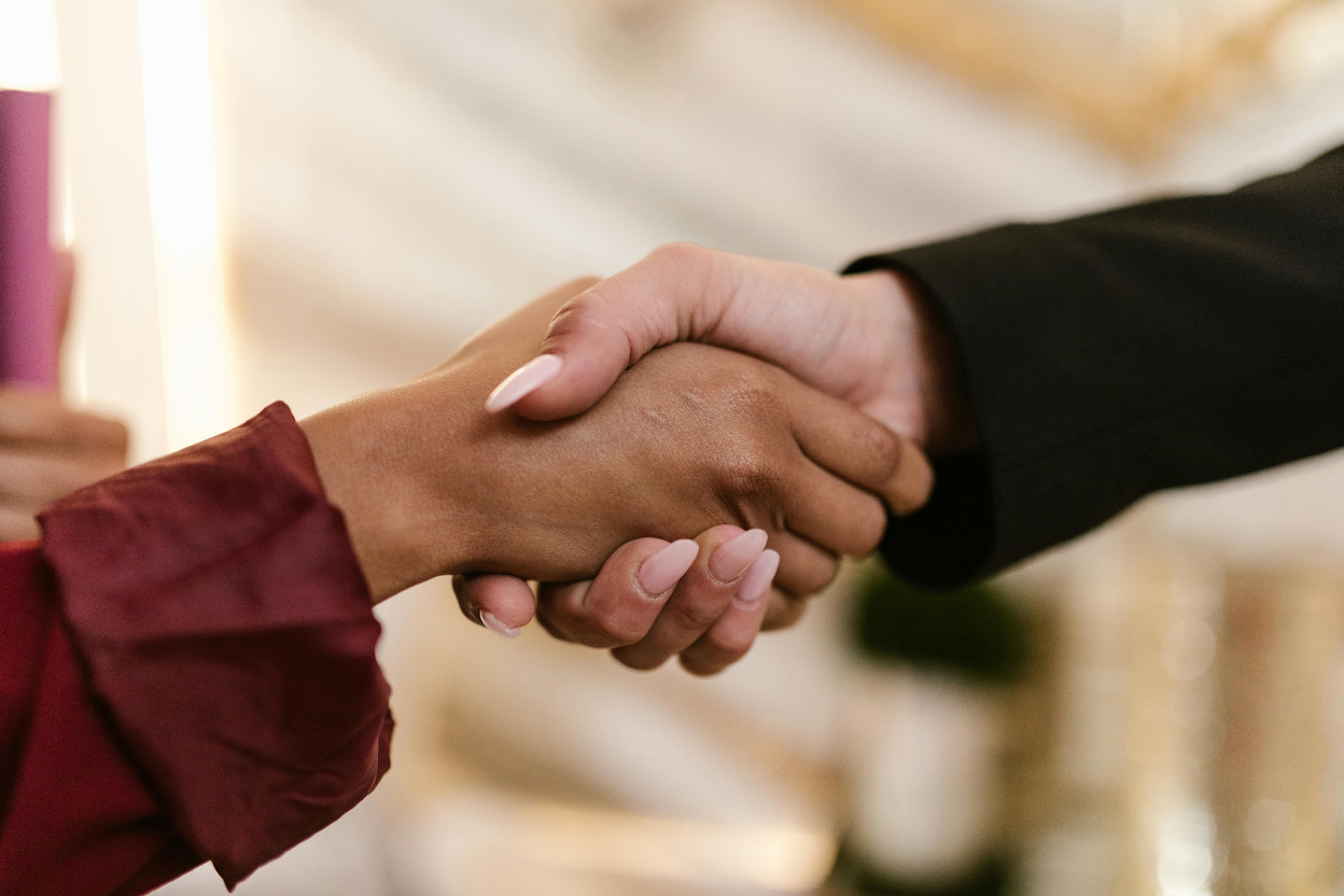 Close-up of two people shaking hands, one in a burgundy sleeve and one in a black sleeve