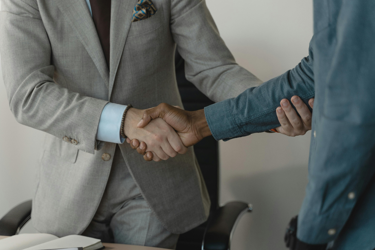 Close-up of two people shaking hands, one in a gray blazer and the other in a teal button-down shirt