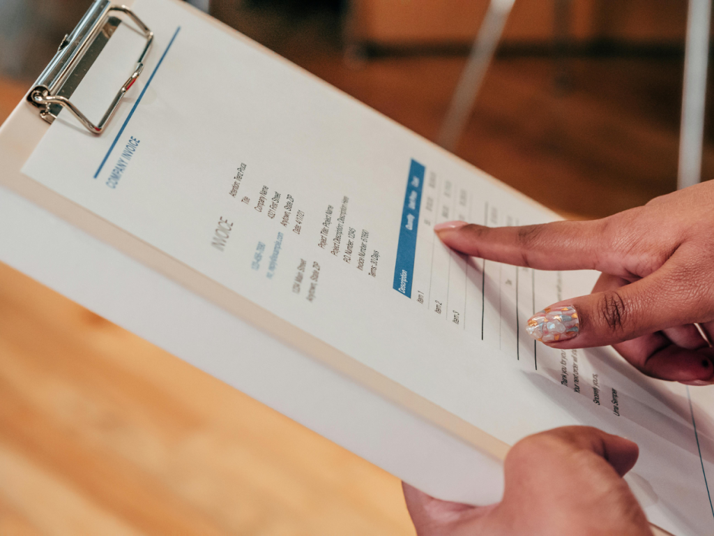 Hands reviewing an open invoice document attached to clipboard on wooden desk