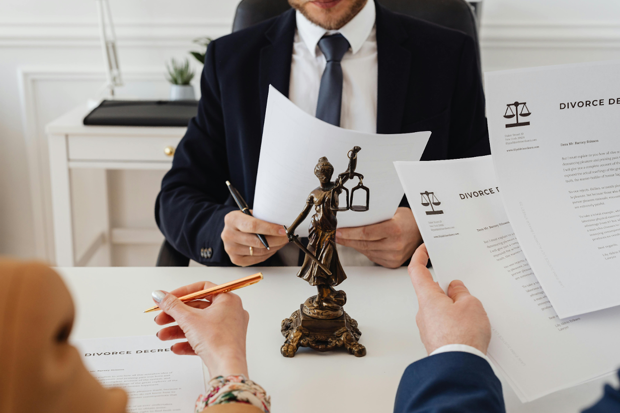 A lawyer reviewing corporate contract documents with clients, with a Lady Justice statue on the desk