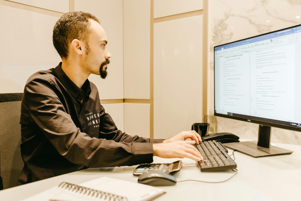 A man typing on a keyboard at a desk, focused on a document displayed on a Dell monitor