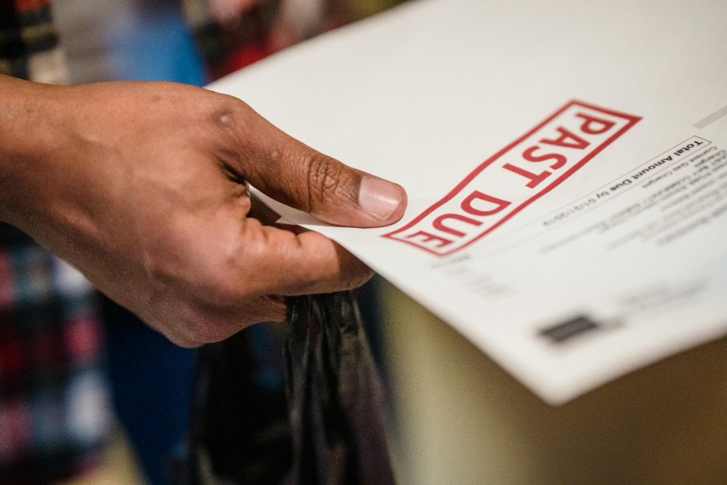 Close-up of a hand holding a document stamped with a red "Past Due" notice