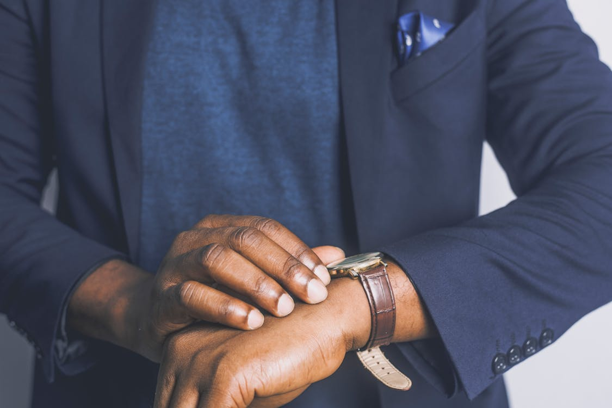 Close-up of a person in a navy suit checking the time on a leather-strap wristwatch