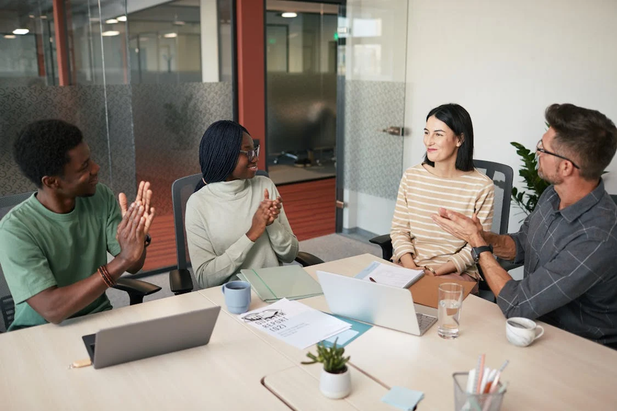 Four diverse colleagues applauding and celebrating together during a meeting in a modern office conference room