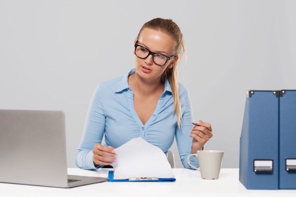 Office worker at a desk reviewing past-due invoices and payment records on a computer screen