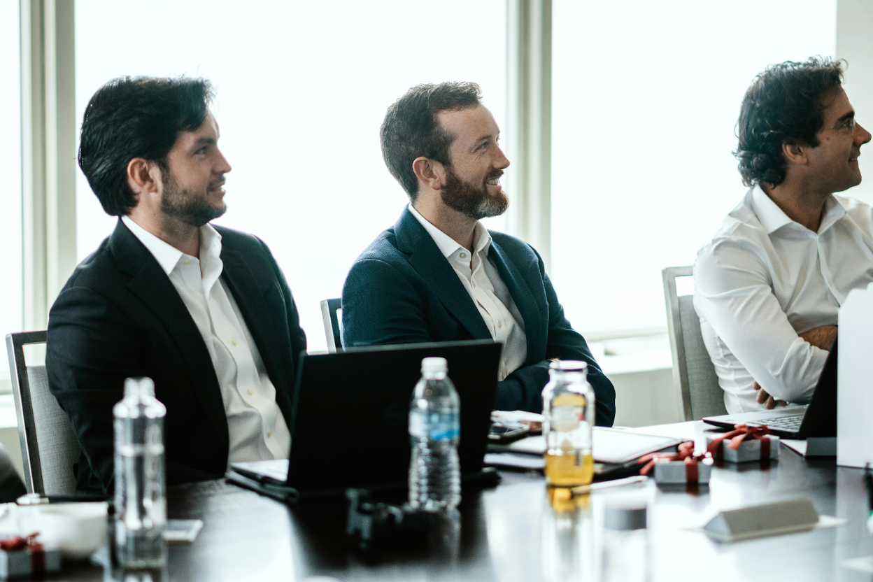 Three business professionals in suits sitting at a conference table during a meeting in a bright office
